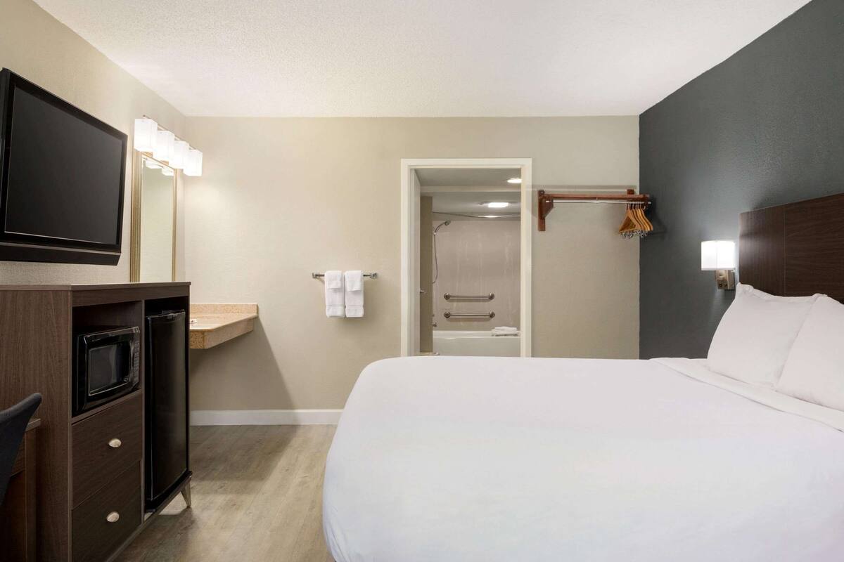 Habitación de hotel con cama, televisor, microondas, escritorio pequeño, tocador con espejo y zona de ducha.