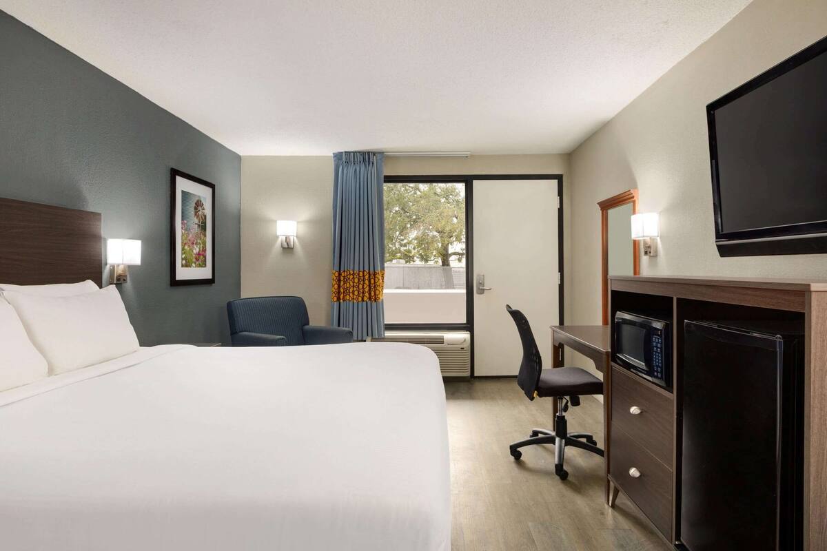 Habitación de hotel con cama, escritorio, silla, televisión y vistas al exterior.