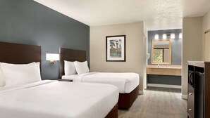 Ein Hotelzimmer mit zwei Betten, einem Badezimmer mit Spiegel und einer kleinen Küchenzeile.