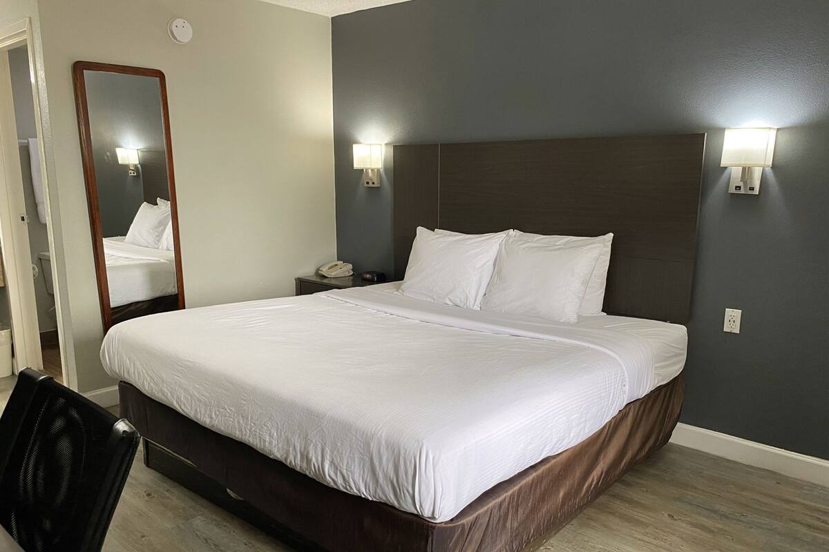 Quarto de hotel com cama grande, mesa de cabeceira, telefone, espelho e luminárias na parede.