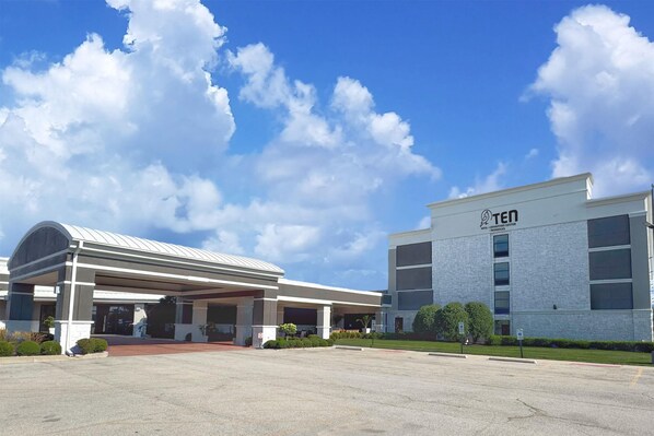 A hotel with a covered entrance, a clear sky, and a building with the 'TEN' logo. - Hotel Gurnee (Gurnee)