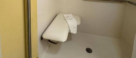 A small, enclosed shower area with a bench and a grab bar.