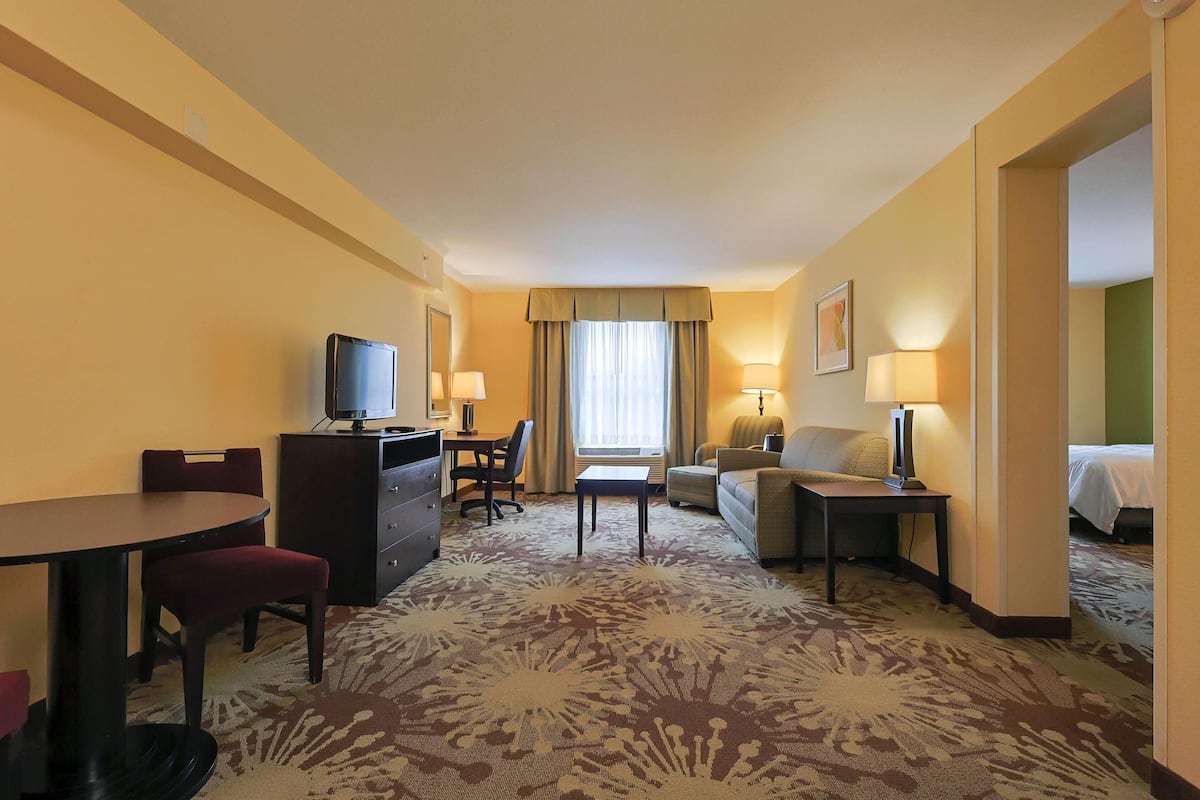 A hotel room with a bed, a desk, a chair, a sofa, a TV, and a lamp.