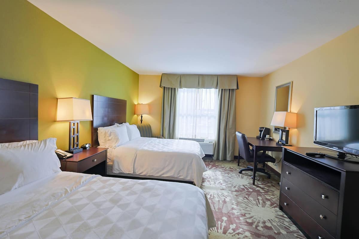 A hotel room with two beds, a desk, a chair, a television, and a dresser.