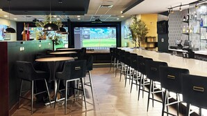 Un espace bar moderne offrant de nombreuses options d’assise, un grand écran diffusant un paysage et un comptoir de bar agrémenté d’un décor à motifs.