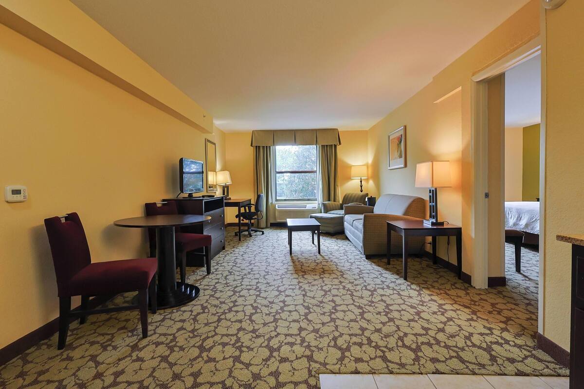 A hotel room with a carpeted floor, a desk with a chair, a sofa, a bed, and a television.