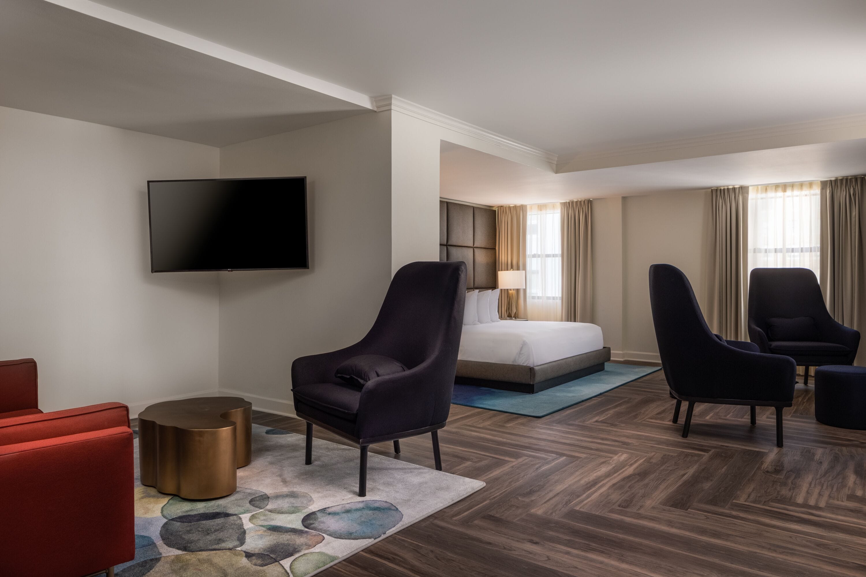 A hotel room with a bed, a flat-screen TV, and two armchairs.