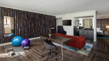 A modern hotel room with a wooden floor, a desk, a red sofa, exercise balls, and a TV.