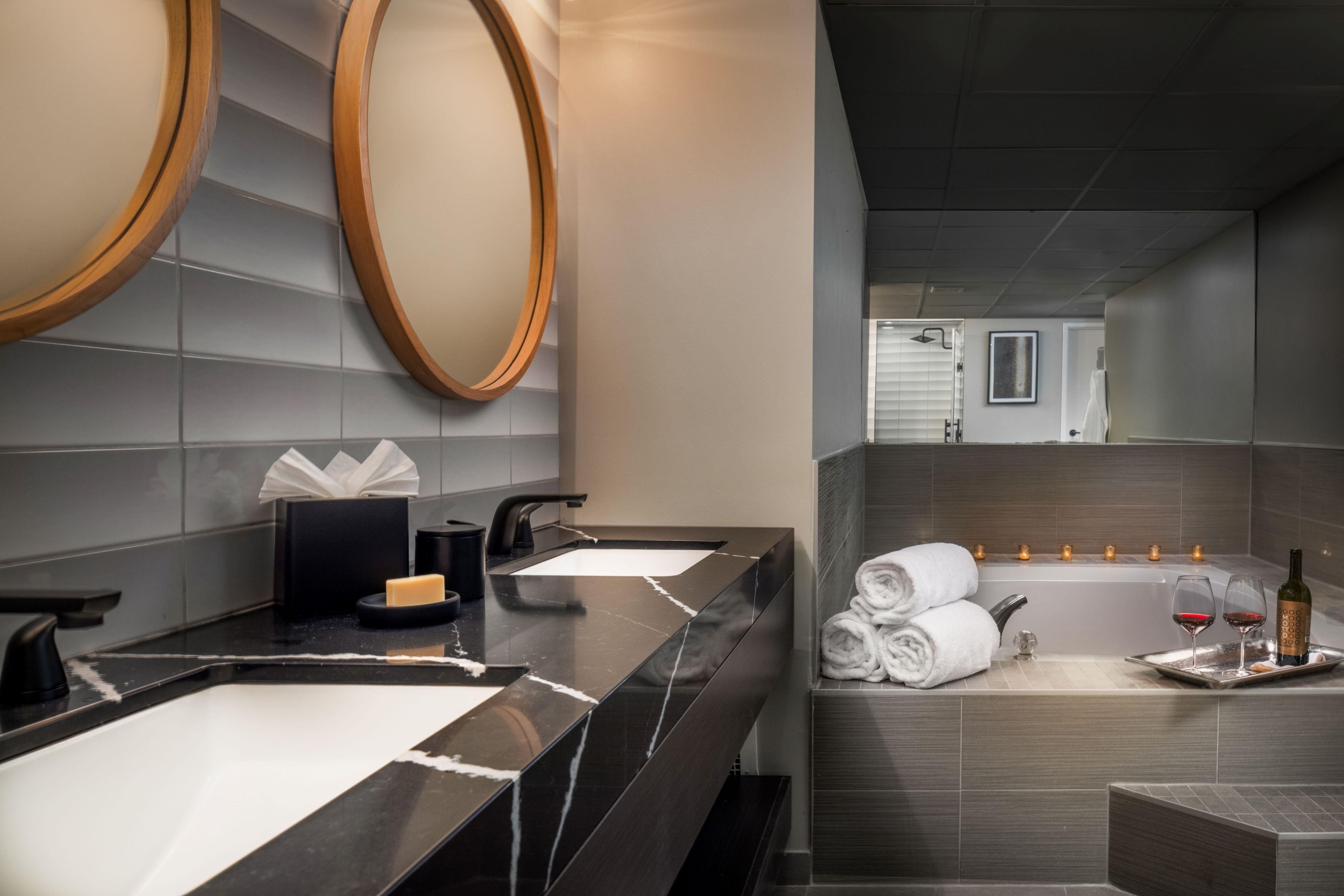 A modern bathroom with two sinks, a large mirror, and a bathtub with candles.