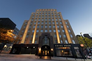 Un hôtel à plusieurs étages, doté d’une entrée imposante, d’une enseigne indiquant « HÔTEL DECO » et d’un ciel dégagé en arrière-plan.