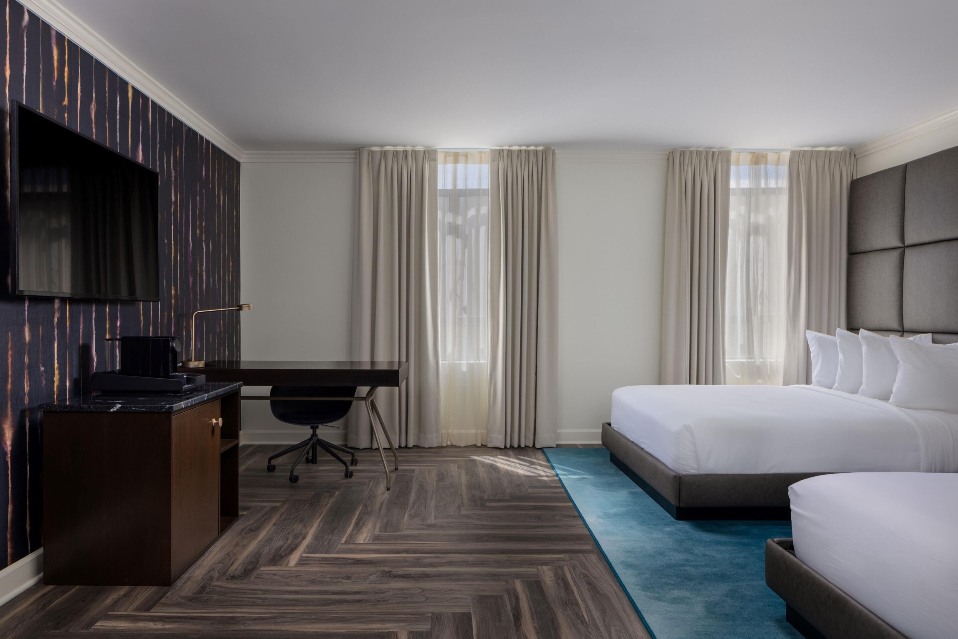 Habitación de hotel con cama, escritorio, silla, televisión y ventana con cortinas.