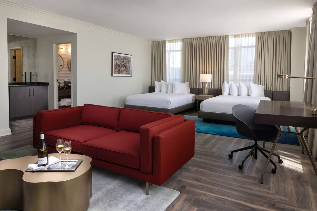 A hotel room with a red sofa, two beds, a desk, and a dining table.