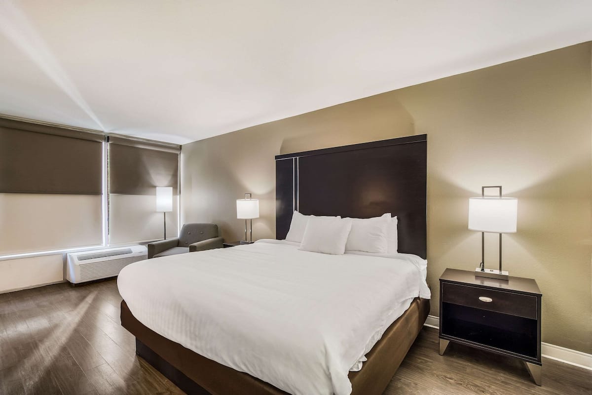 Quarto de hotel com uma cama grande, mesas de cabeceira, aquecedor e janela com persianas.