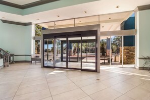 A spacious lobby with a modern glass door entrance, a staircase, and a view of the outdoor area.
