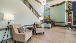 A spacious lobby with a high ceiling, a staircase, and a view of trees through large windows. - Clarion Inn & Suites Florence - Darlington (Florence)