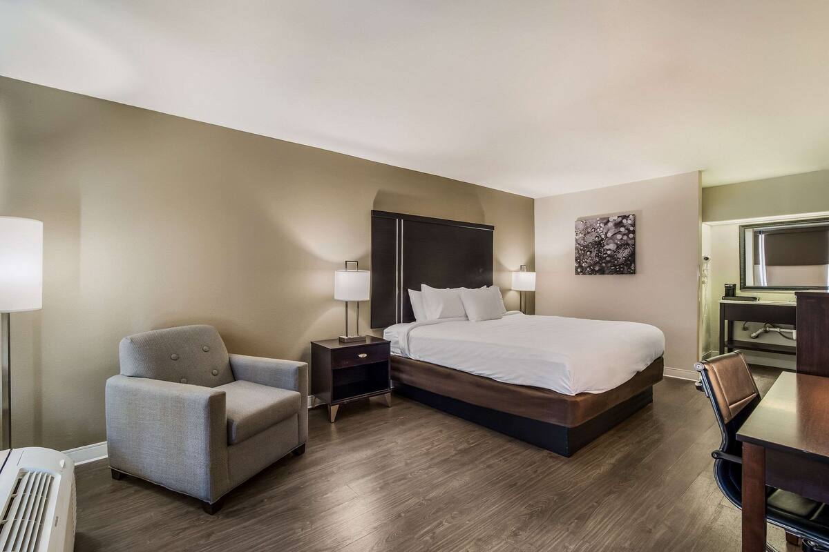 Quarto de hotel com uma cama, duas poltronas, uma escrivaninha e um abajur.
