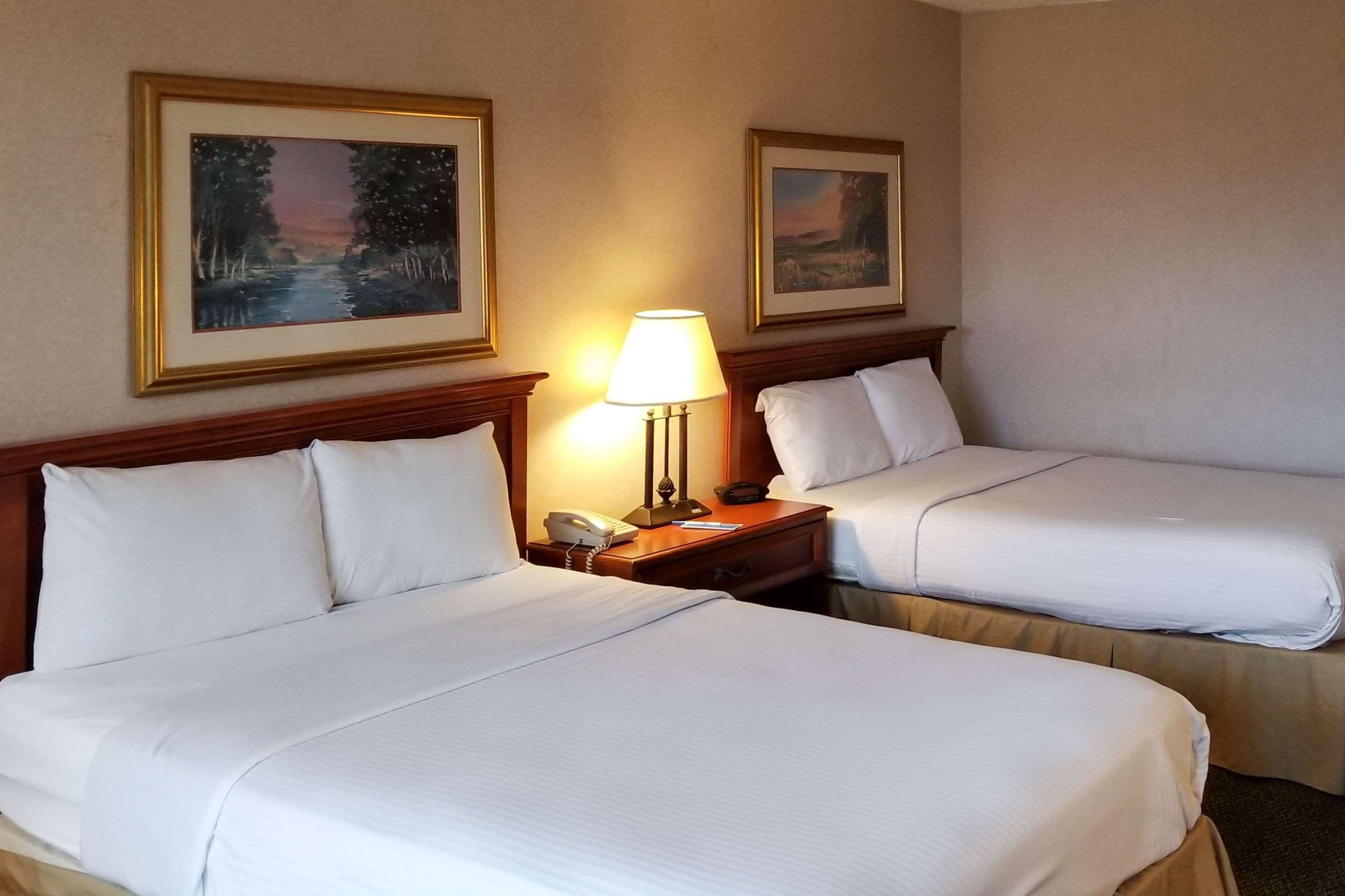 Two adjacent beds with white linens, a bedside lamp, a phone, and two framed landscape paintings on the wall.