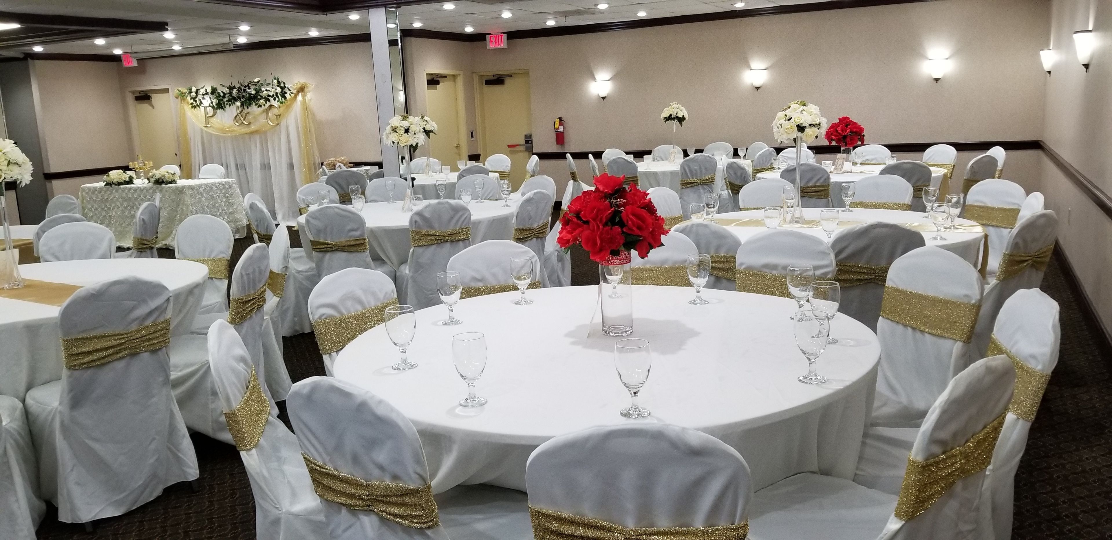 Un salón de banquetes con mesas redondas, manteles blancos y sillas adornadas con cintas doradas.