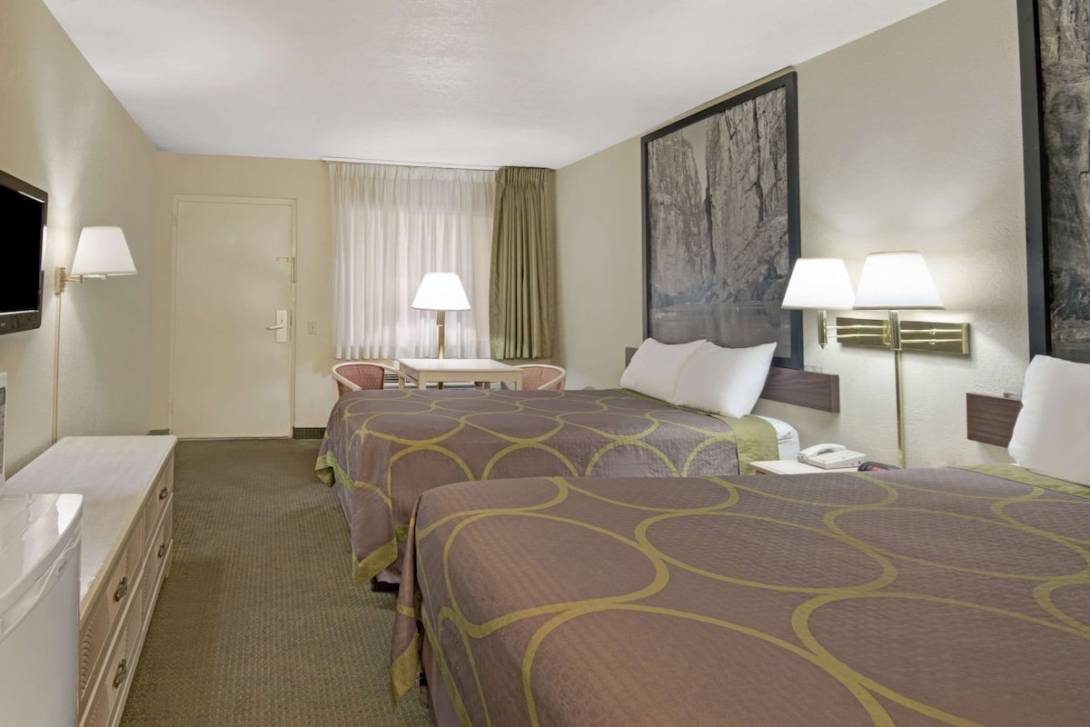 A hotel room with two beds, a desk, a chair, a TV, and a painting on the wall.