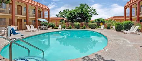 A pool area with lounge chairs and a building with a red roof.