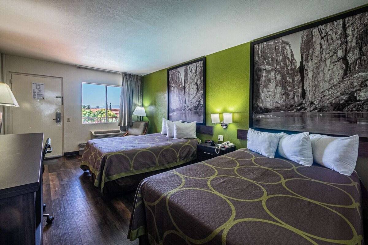 A hotel room with two beds, a desk, a chair, a window with a view, and artwork on the walls.