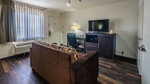 A hotel room with a brown sofa, a desk with a lamp, a television, and a minibar. - Super 8 by Wyndham El Paso Airport (El Paso)