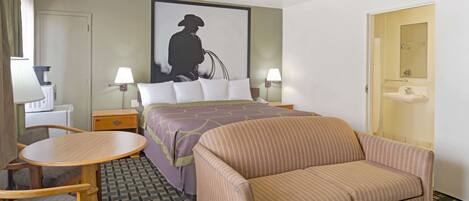 A hotel room with a bed, a sofa, a small table, two chairs, a desk, a lamp, a painting, and a bathroom door.
