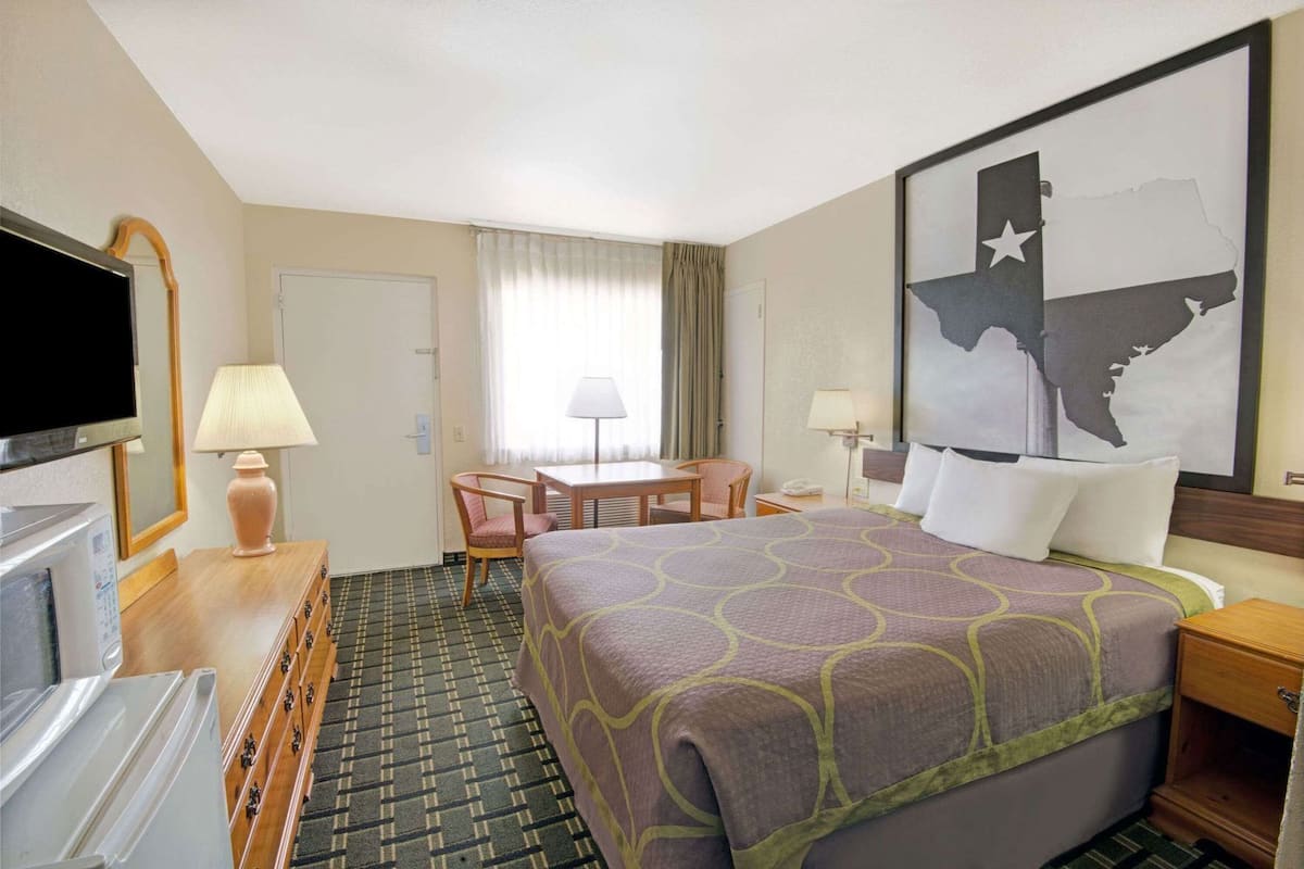 A hotel room with a bed, a desk, a chair, a TV, and a map on the wall.