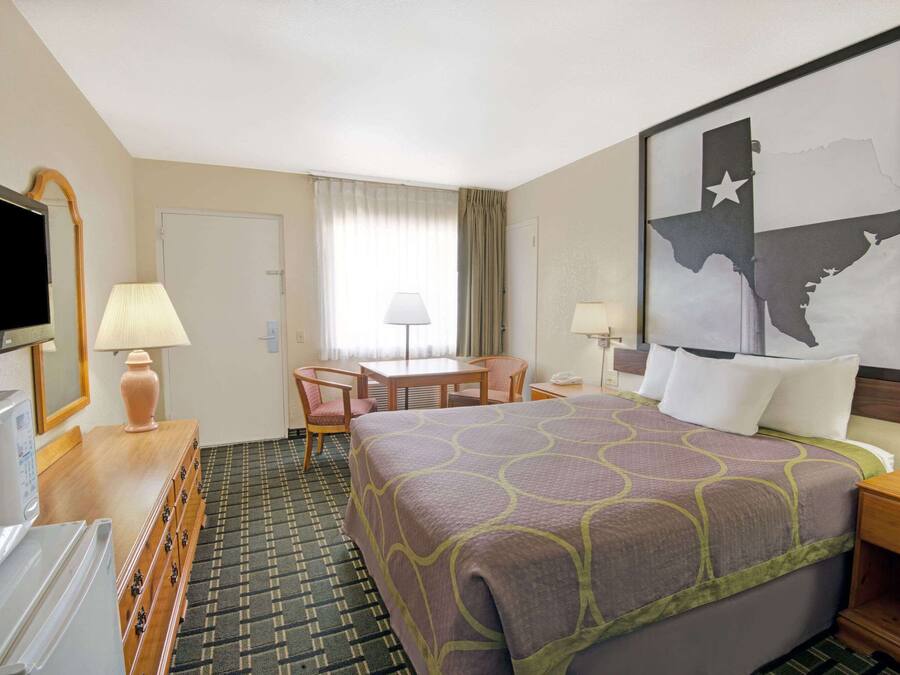 A hotel room with a bed, a desk, a chair, a TV, and a large wall map.