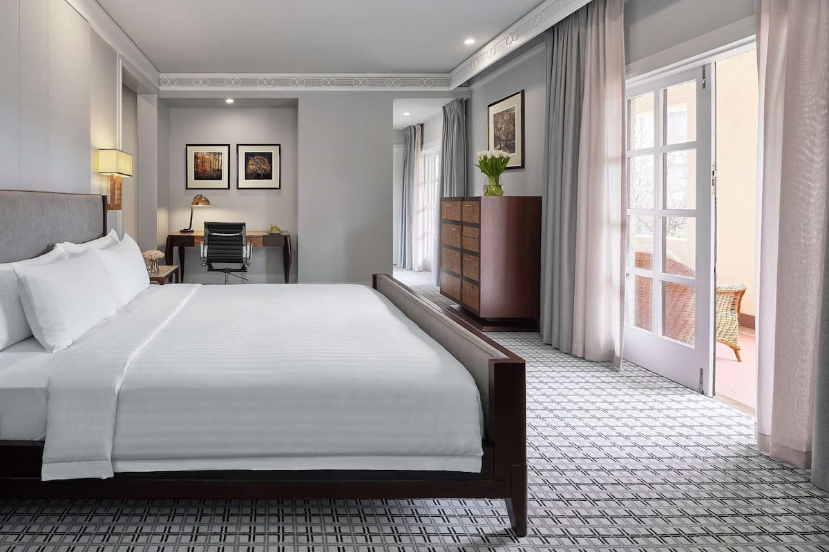 Een hotelkamer met een groot bed, een bureau met stoel, een garderobe en uitzicht op het balkon.