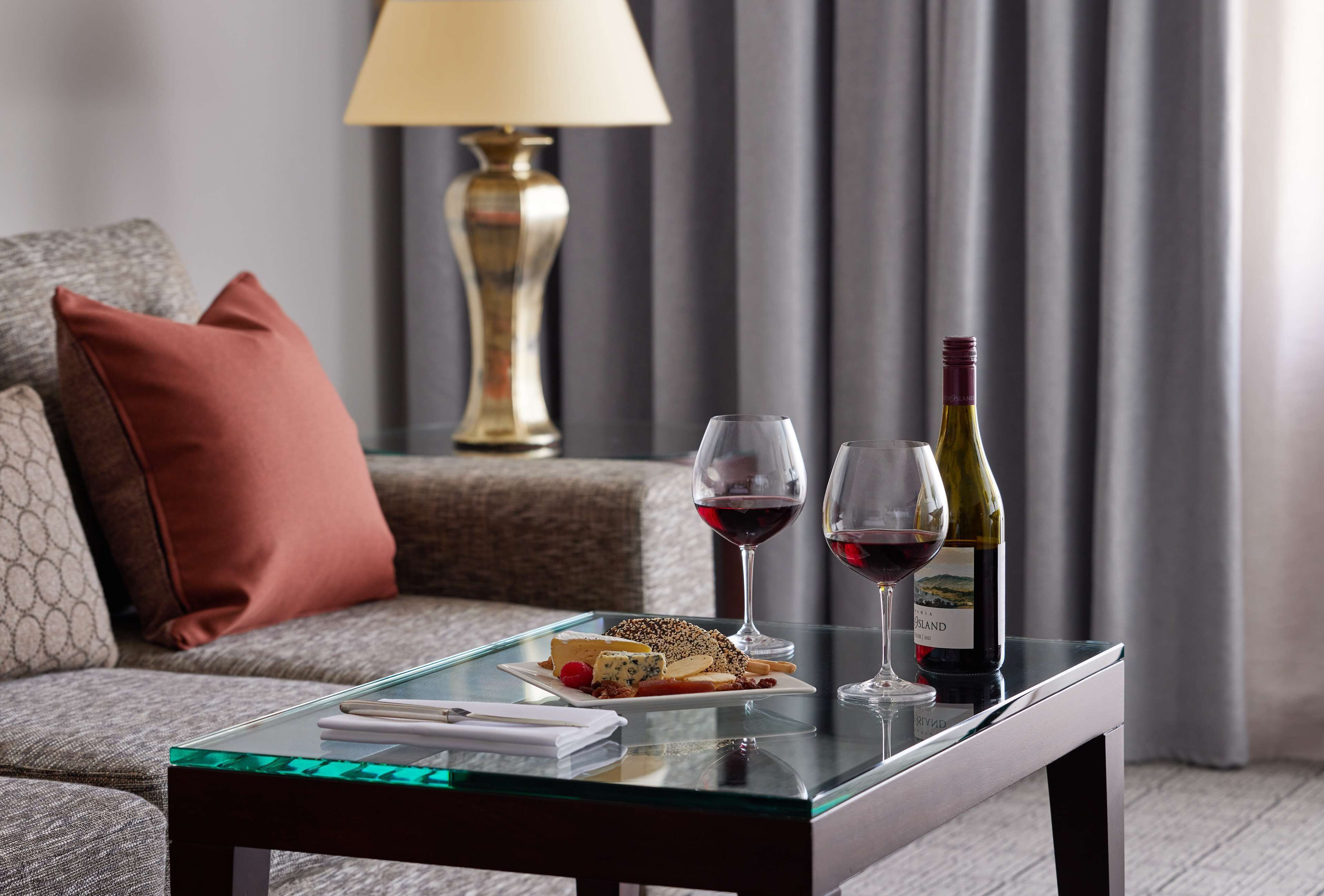 A glass-top table with a plate of cheese and crackers, two wine glasses, and a bottle of wine.