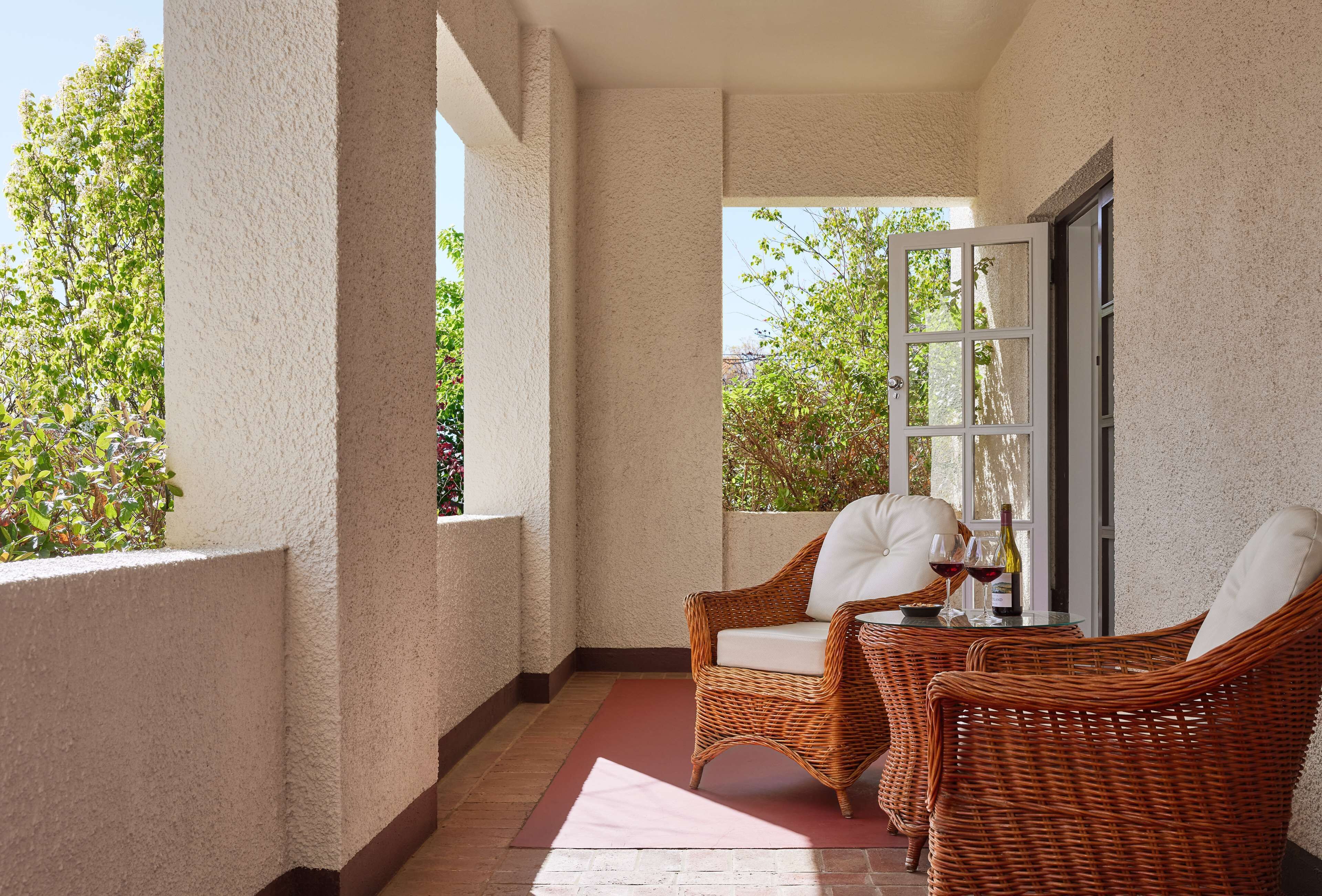 Ein Balkon mit Korbstühlen und einem Tisch, ein Fenster mit Blick auf Grünflächen und eine Tür.