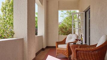 Ein Balkon mit Korbstühlen und einem Tisch, ein Fenster mit Blick auf Grünflächen und eine Tür.