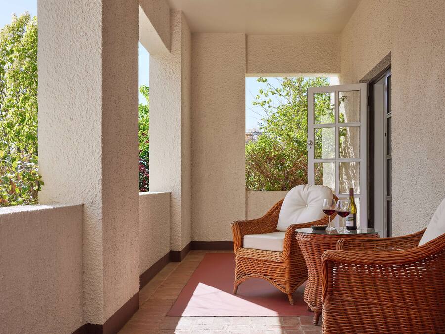 Ein Balkon mit Korbstühlen und einem Tisch, ein Fenster mit Blick auf Grünflächen und eine Tür.