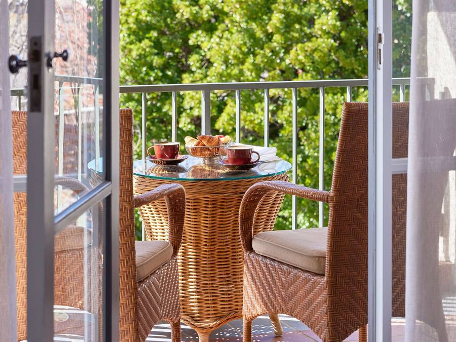 A balcony with wicker furniture, a glass table, and a view of greenery.