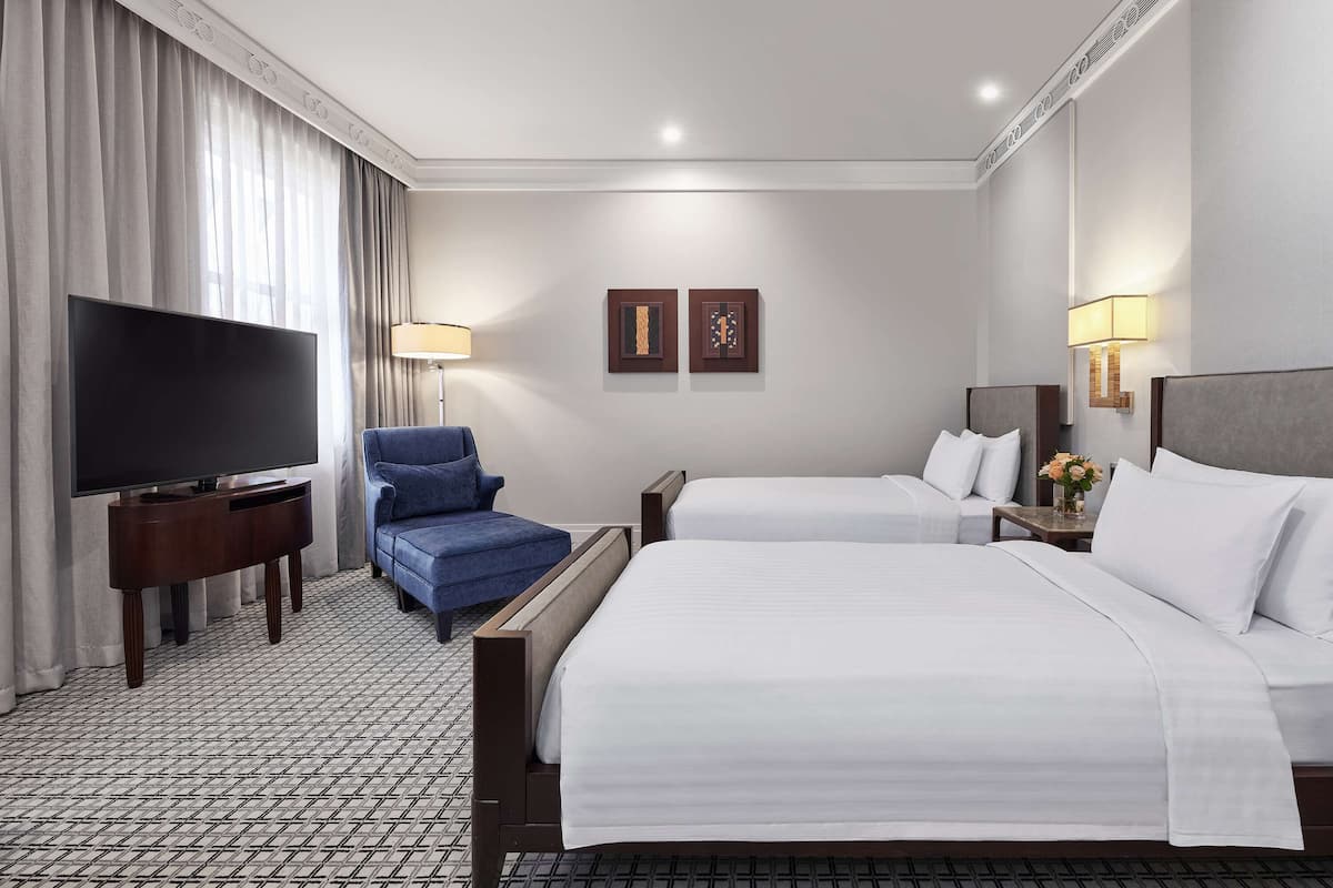 Een hotelkamer met twee bedden, een televisie, een blauwe fauteuil en een klein tafeltje met een lamp.