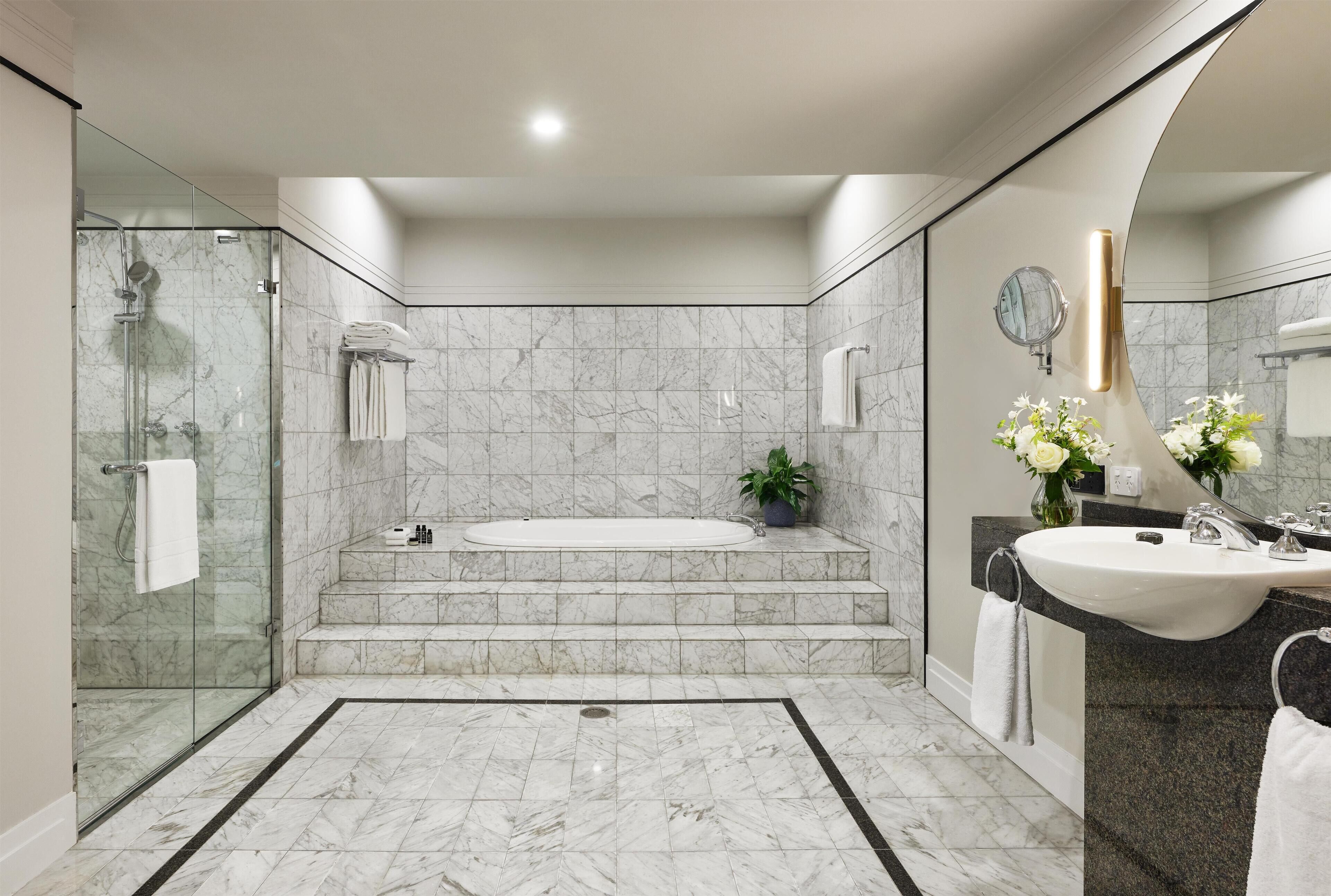 A modern bathroom with a glass-enclosed shower, a freestanding bathtub, a vanity with a sink, and a large mirror.
