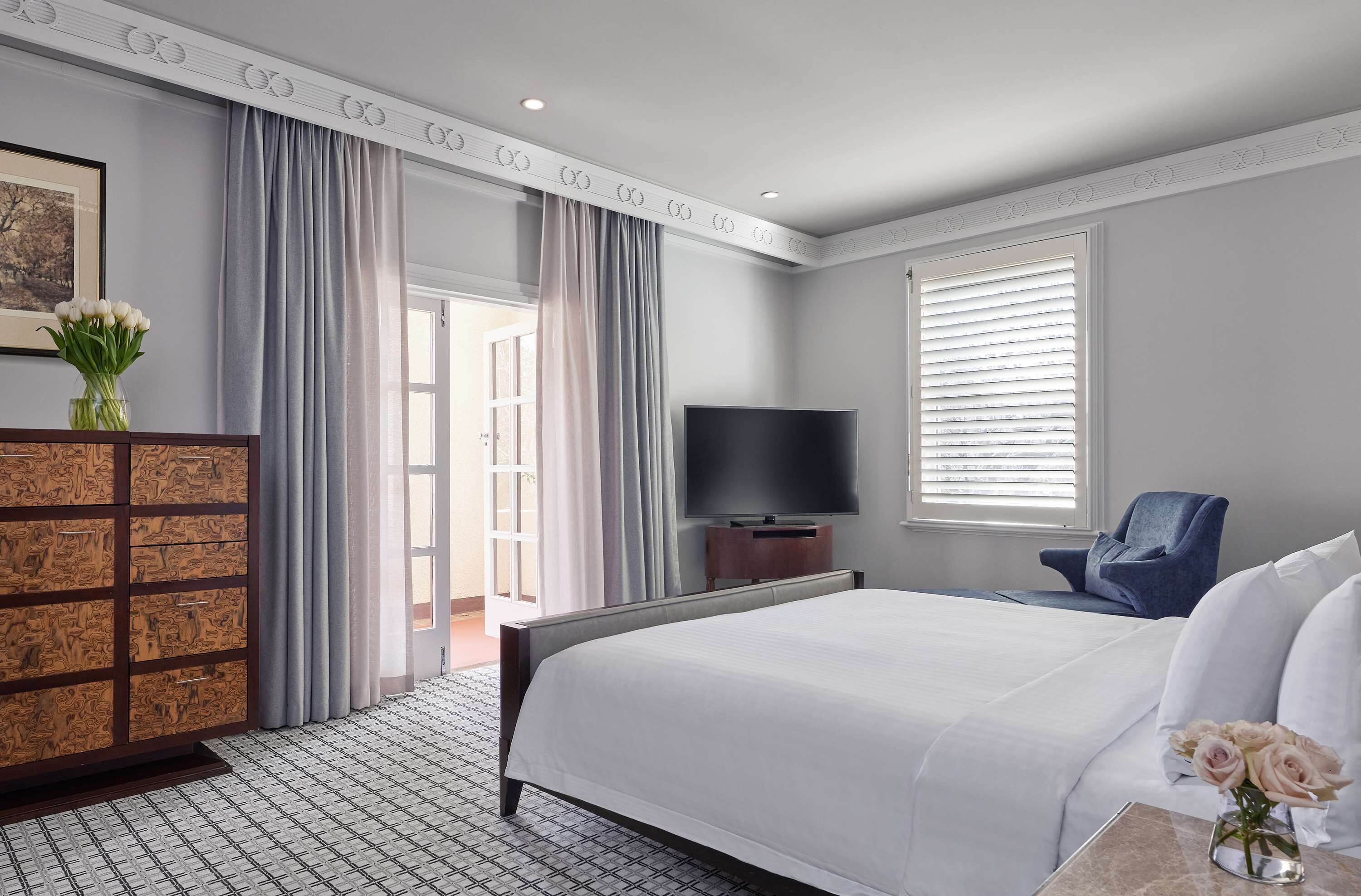 A hotel room with a large bed, a TV, a chair, and a dresser.