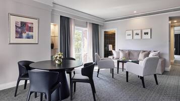 A modern hotel room with a dining area, a sofa set, and a large window with curtains.