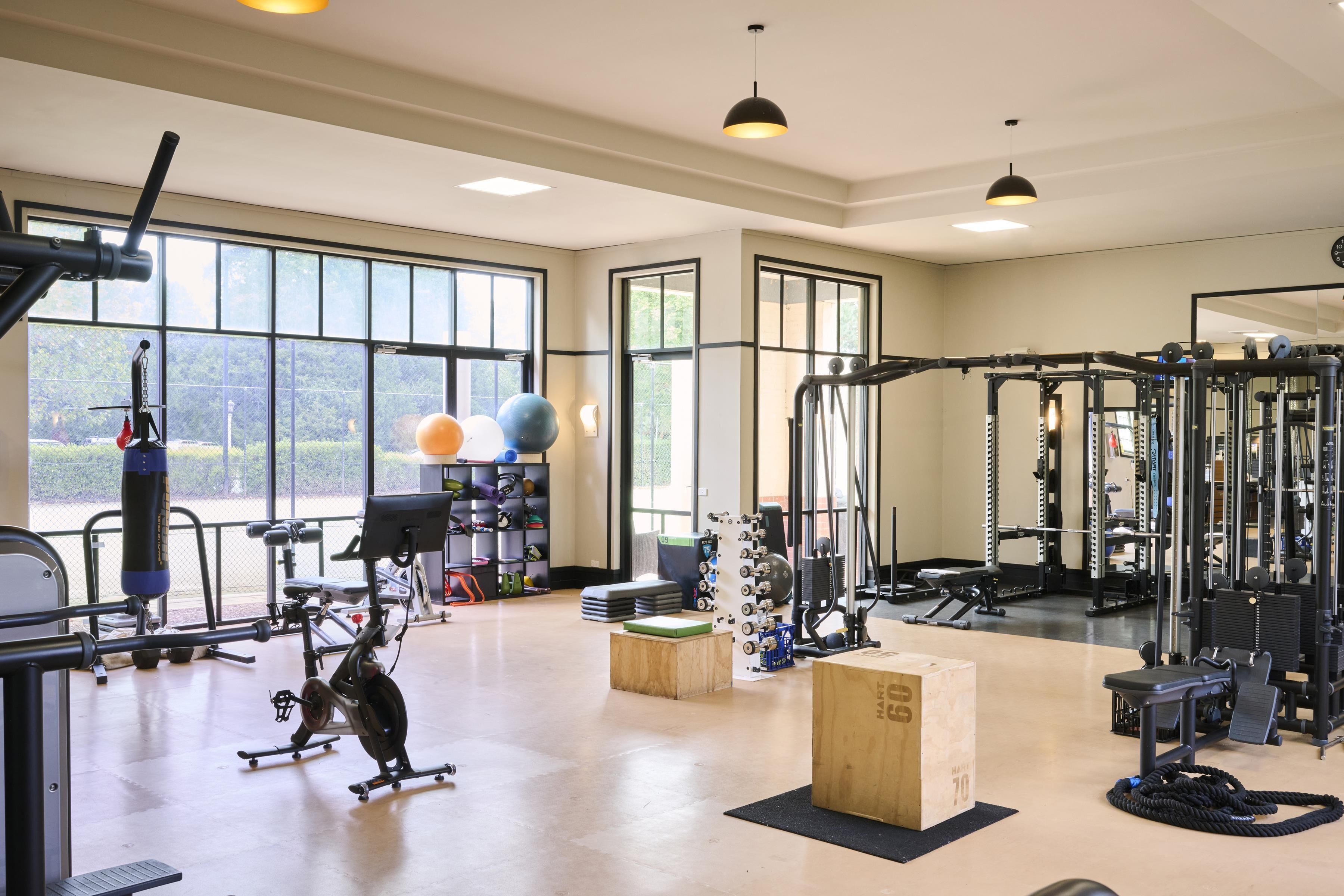 A gym with various exercise equipment, large windows, and a view of greenery outside.