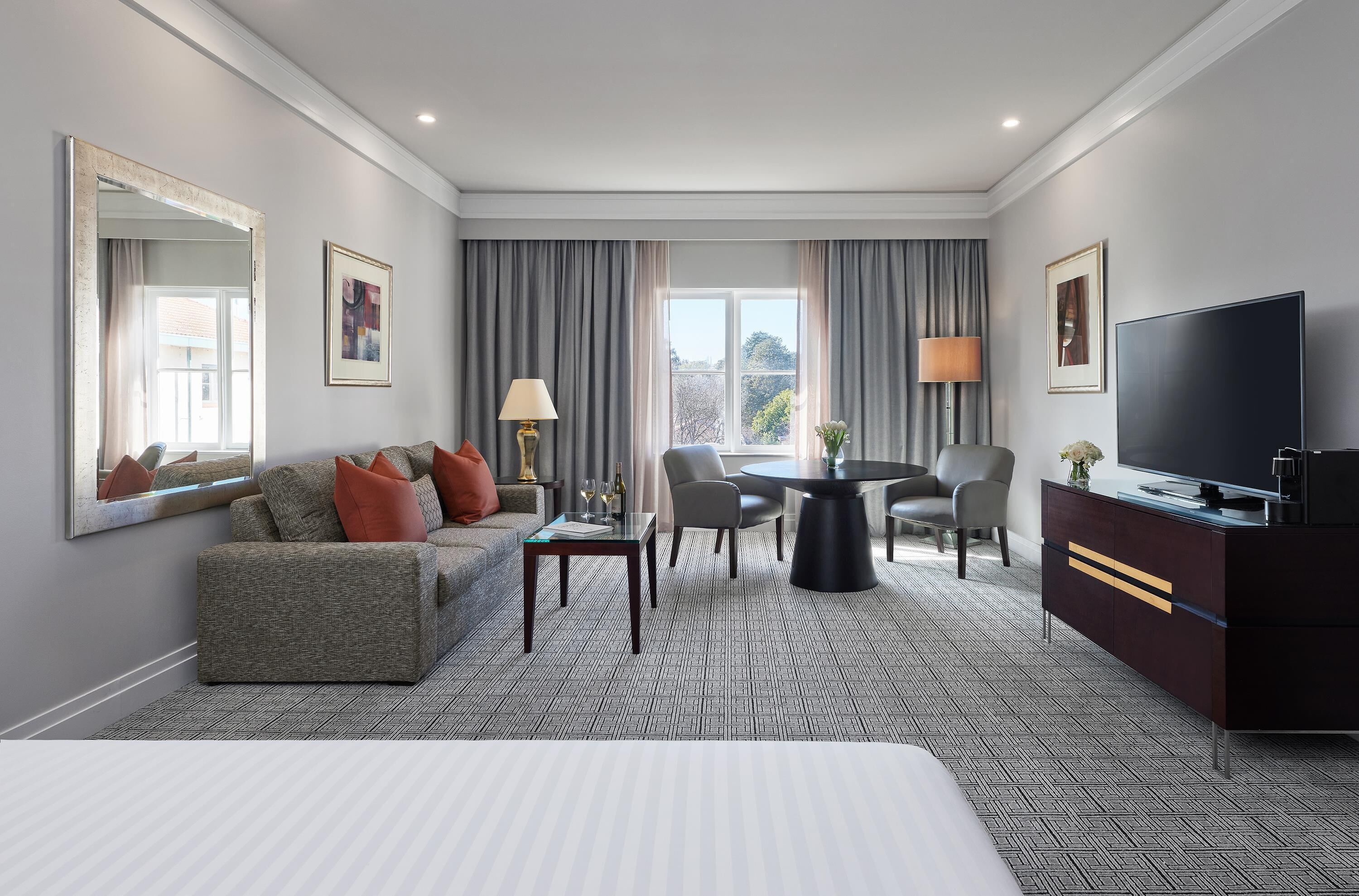 A hotel room with a large bed, a sofa, a dining table, and a TV.