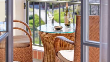 A wicker table with a glass top, two wine glasses, and a bottle on a balcony.