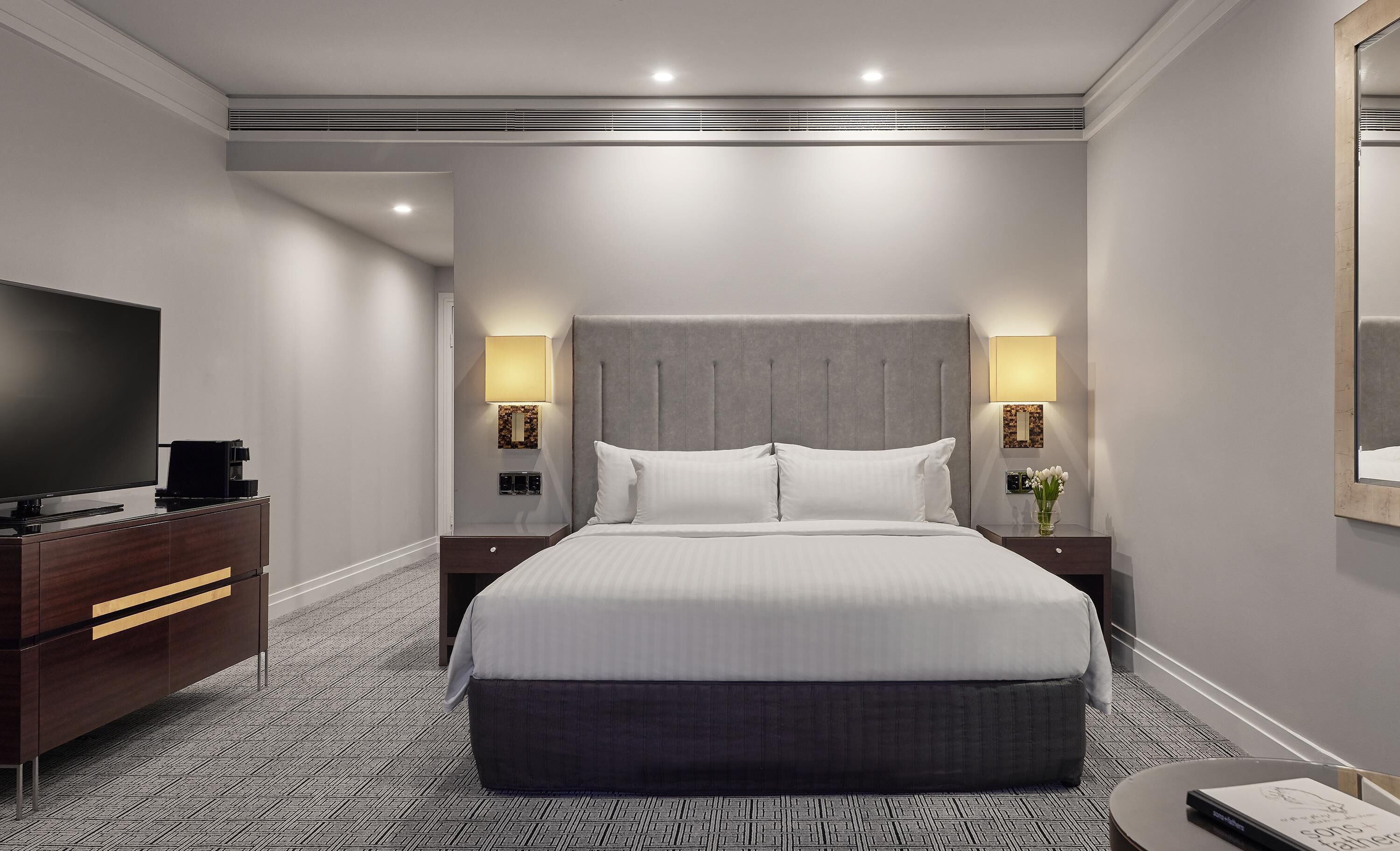 Ein Hotelzimmer mit einem großen Bett, einem Fernseher, einer Kommode und zwei Nachttischlampen.