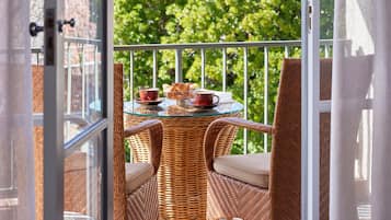 Un balcón con mobiliario de mimbre, una mesa de vidrio y vistas a la vegetación.
