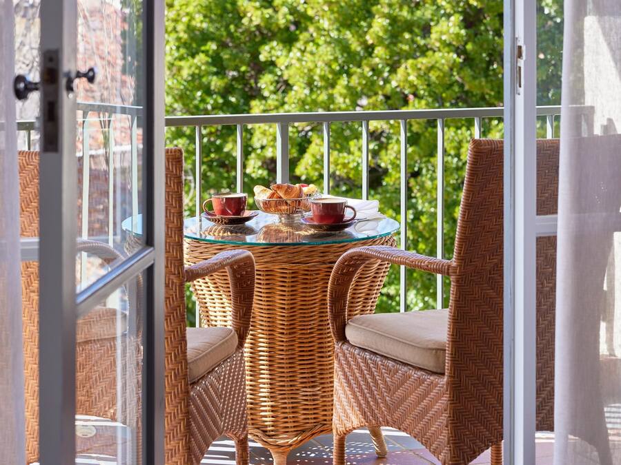 Un balcón con mobiliario de mimbre, una mesa de vidrio y vistas a la vegetación.