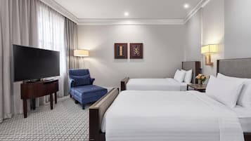 Habitación de hotel con dos camas, un televisor de pantalla plana, un sillón azul y dos lámparas de pared.