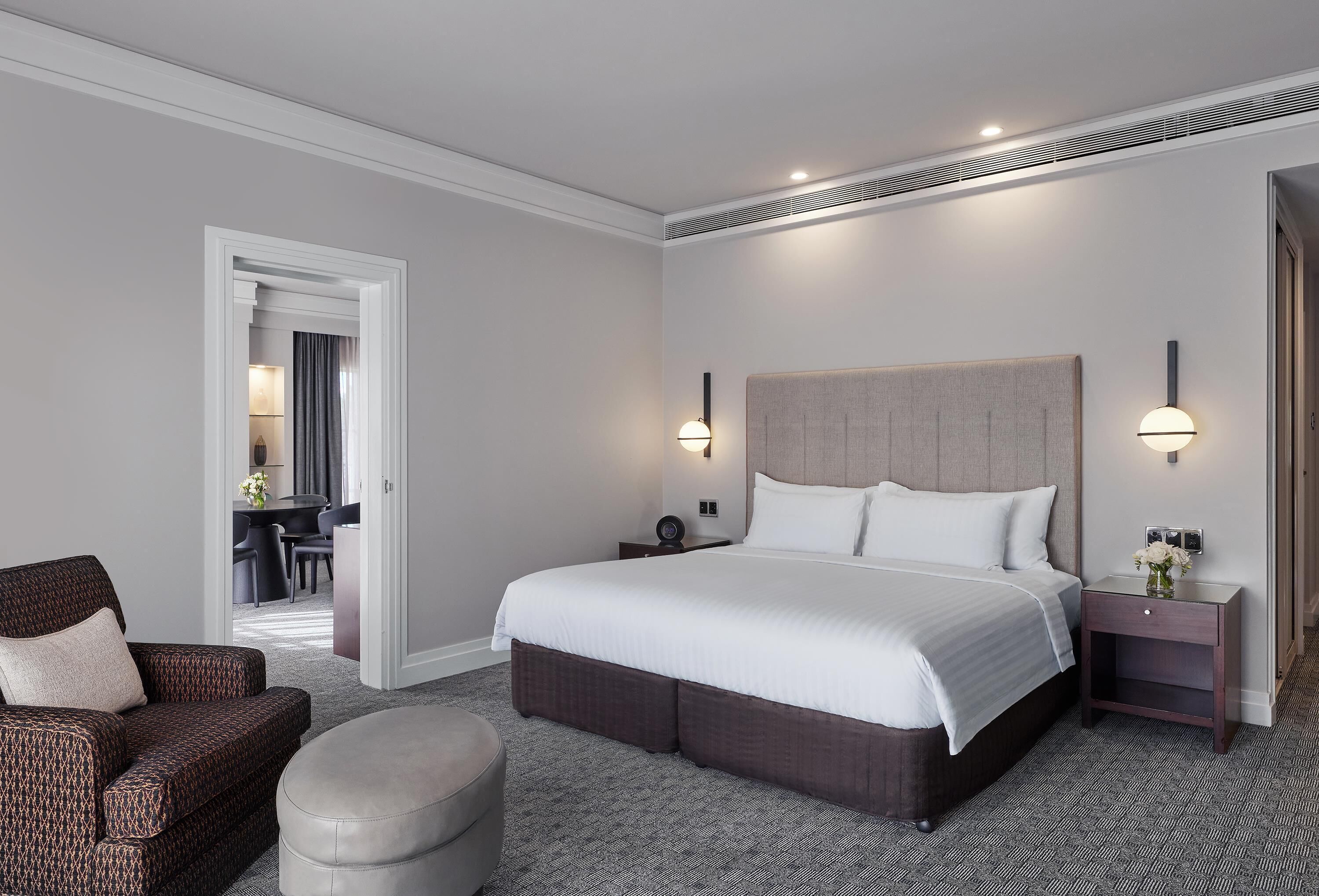 A hotel room with a large bed, a sofa, a nightstand, and a chair.