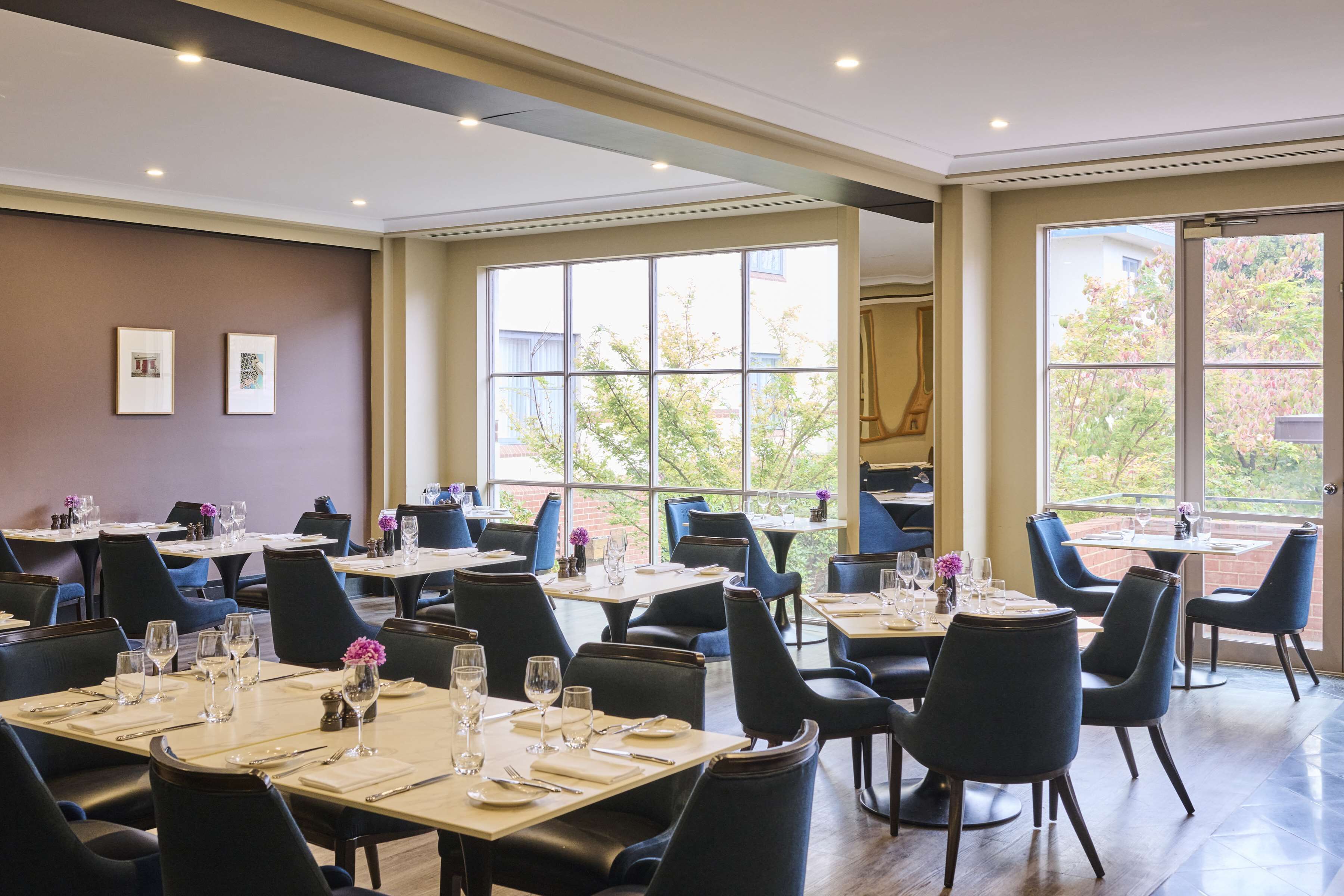 Een restaurant met meerdere tafels en stoelen, grote ramen en afbeeldingen in lijsten aan de muur.