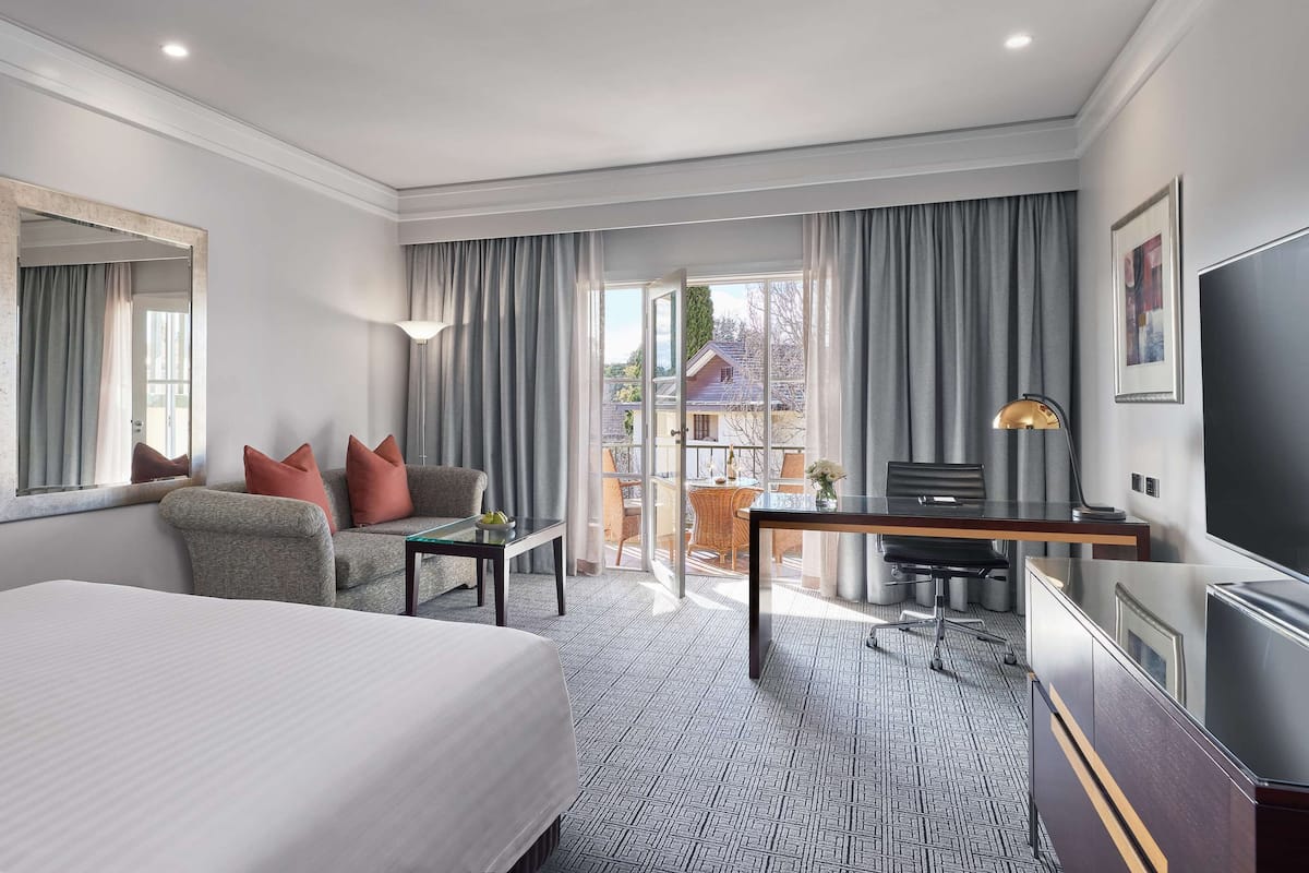 Hotelkamer met een groot bed, een bureau met stoel, een televisie en een balkon met gordijnen.