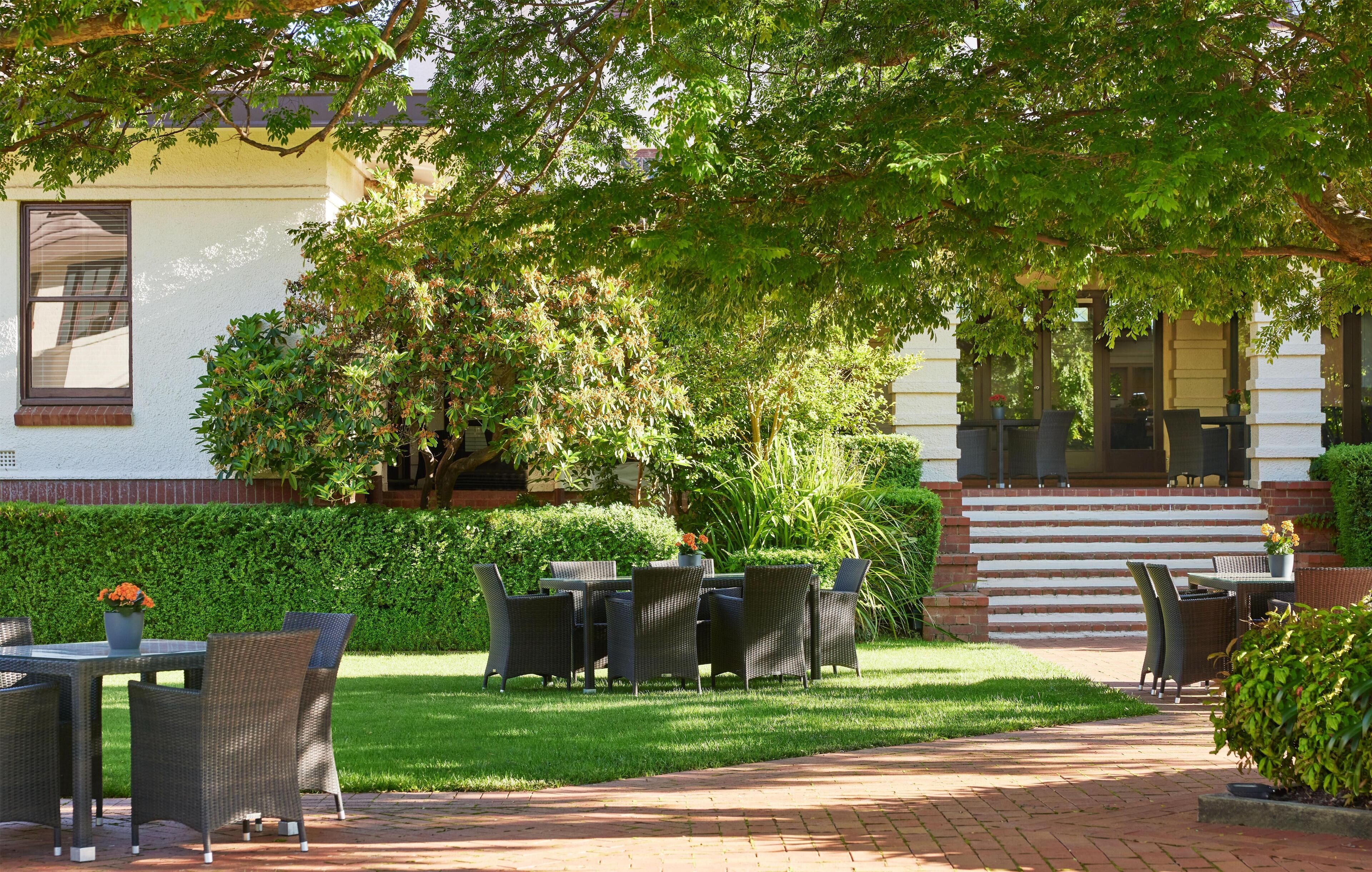 An outdoor patio with wicker furniture, a brick pathway, and a building with steps leading up to a door.
